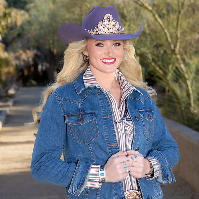 Miss Rodeo America, Callie Mueller, with blonde hair, wearing a purple hat and denim jacket, and smiling, posing for the camera.